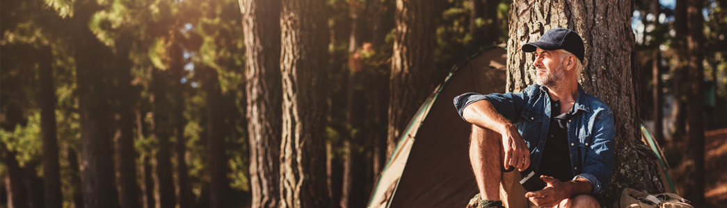 Happy man sitting under a tree, with a tent in the background.